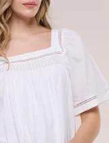 Blusa de corte holgado color marfil, confeccionada en mezcla de modal y algodón, con escote cuadrado y mangas cortas adornadas con detalles de puntilla calada.