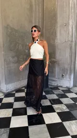 Falda larga de encaje negro con diseño de capas, presentando una sección superior opaca y una sección inferior transparente con terminación de volado en el ruedo.