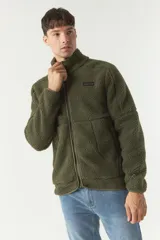 Campera de sherpa color verde militar, con cierre frontal completo, cuello alto y bolsillos laterales con cierre. Presenta un parche pequeño con logo en el pecho.