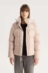Campera puffer corta color beige con capucha desmontable, cierre frontal con cremallera y botones a presión, y cordón ajustable en el ruedo. Diseño acolchado con bolsillos laterales.