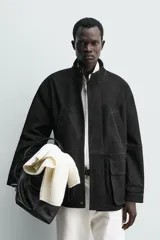 Parka de cuero color negro, de corte relajado, con cuello alto, cierre frontal con cremallera oculta y solapa con botones a presión. Cuenta con bolsillos frontales tipo cargo con solapa en la cadera y bolsillos de vivo en el pecho.
