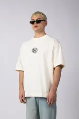 Remera color crema de corte oversize con logo bordado en el pecho y parche estampado en la espalda.