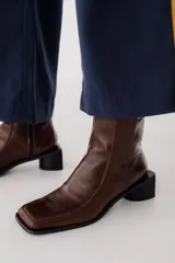 Bota corta de cuero color bordó, con punta cuadrada y taco bloque bajo. Cierre lateral con cremallera.