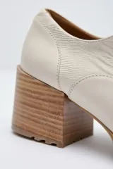 Zapato de cuero color beige, con taco de madera y suela dentada. Presenta un diseño slip-on con detalles de textura en relieve en los laterales y el empeine.