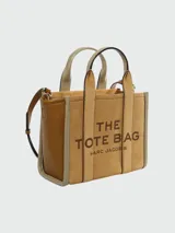 Cartera tipo tote de Marc Jacobs, confeccionada en una combinación de gamuza y cuero texturizado en tonos tierra. Presenta el logo 'THE TOTE BAG' estampado en el frente, doble asa superior y correa ajustable extraíble.