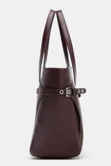 Bolso tipo shopper de gran tamaño en color bordó, con diseño estructurado y detalles de correas laterales con ojales metálicos y hebillas. Cuenta con doble asa de mano y cierre superior mediante imán.