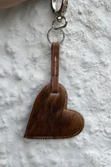 Llavero con dije en forma de corazón confeccionado en cuero con pelo, con costuras a la vista y gancho metálico.