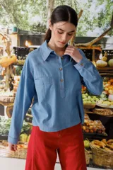 Blusa celeste de denim con cuello polo, manga larga y botones marrones.