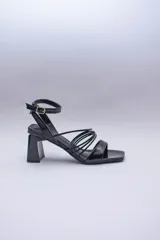 Sandalias negras de cuero sintético con tiras finas cruzadas en el empeine, pulsera al tobillo con hebilla y taco geométrico.