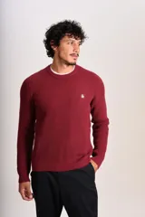 Sweater de punto grueso en color bordó, con cuello redondo, mangas largas y puños acanalados. Presenta un pequeño logo bordado en el pecho.