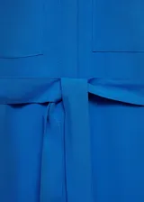 Vestido midi de corte camisero color azul vibrante, confeccionado en mezcla de lyocell y lino. Presenta cuello camisero, cierre frontal con botones, mangas largas con puños abotonados y dos bolsillos de parche en el pecho. Incluye un lazo ajustable en la cintura para entallar la silueta y aberturas laterales en el bajo.