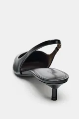 Zapato destalonado de piel negro, con punta fina y tacón kitten bajo y curvo. Posee una tira trasera con pieza elástica para ajuste en el talón.