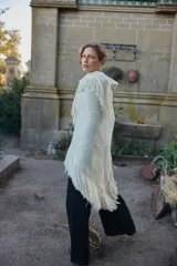 Poncho triangular color crema con maxi flecos, confeccionado con una mezcla de lana merino, mohair, viscosa, algodón y otras fibras. Presenta un mix de texturas que incluye lurex y un hilado teñido a mano con lentejuelas.