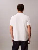 Chomba blanca de piqué de algodón, corte clásico, cuello tradicional, cartera de botones y bajo con aberturas laterales. Tiene un logo bordado en el pecho.