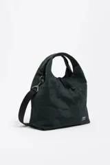 Bolso bandolera de estructura blanda marca Bimba y Lola, confeccionado en nylon con detalles en cuero. Presenta doble asa de mano, correa de tejido regulable y extraíble, cierre de cordón y logo metálico en el frente.