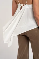 Blusa blanca de satén, corte al cuerpo con escote en V y tirantes finos. Presenta un diseño cruzado en los laterales con tiras largas para atar.