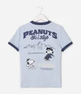 Remera de algodón color celeste con cuello y bordes de mangas en color azul marino. Presenta estampa frontal con el personaje Snoopy vestido con campera puffer y la inscripción Peanuts Ski Lodge.