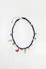 Collar corto de tela azul marino tipo organza, decorado con múltiples charms colgantes que incluyen dijes de peces metálicos, un coral rojo, cuentas de vidrio de colores, perlas y elementos metálicos dorados. Cuenta con cadena de alargue y cierre de mosquetón.