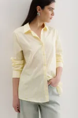 Camisa de corte clásico con cuello camisero, mangas largas con puños abotonados y cierre frontal con botones. Presenta un diseño a rayas verticales finas en tonos amarillo y blanco.