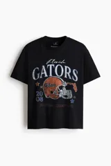 Remera de algodón negro con hombros caídos y cuello redondo. Estampado frontal estilo universitario con la inscripción 'Gators', casco de fútbol americano e insignias conmemorativas.