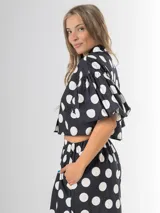 Conjunto de dos piezas con estampa polka dots en negro y blanco, compuesto por un pantalón tipo culotte de tiro alto con bolsillos y una blusa estilo camisa con mangas globo y cierre frontal de botones.