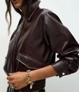 Campera bomber de cuero sintético color marrón oscuro, con cuello camisero, cierre frontal con botones metálicos y elástico en el ruedo.