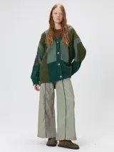 Cardigan oversize de tejido de punto grueso con diseño de bloques de color en tonos tierra. Presenta cuello en V, cierre frontal con botones, mangas largas con terminación abullonada y parches decorativos en el pecho y hombro.