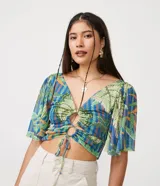Blusa cropped con estampado de hojas en tonos verdes y azules, escote en V, mangas acampanadas y lazo ajustable en el busto.