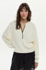 Sweater de tejido de punto color blanco marfil, con calce relajado, mangas largas levemente abullonadas, escote en V con botones y detalles de ribetes en color negro.