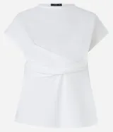 Blusa de manga corta color blanco hueso, con cuello redondo y un detalle de cruce o drapeado asimétrico en la parte delantera a la altura de la cintura. La tela presenta una textura sutil.