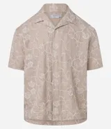 Camisa de poliéster color beige con bordado floral blanco, de corte regular, cuello inglés, manga corta y abotonada en el frente.