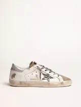 Zapatillas urbanas Golden Goose modelo Super-Star, de cuero blanco con efecto desgastado. Presentan una estrella de animal print en el lateral, talón plateado y cordones grises con inscripciones.