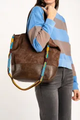 Bolso tipo shopper de tamaño maxi, confeccionado en material efecto gamuza marrón con base en cuero sintético oscuro. Cuenta con una correa ajustable y desmontable trenzada en varios colores.