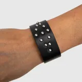 Brazalete ancho de cuero vegano negro con tachas metálicas semiesféricas plateadas distribuidas en la superficie.