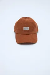 Gorra de pana azul marino con visera curva, parche frontal con texto y pequeño bordado rojo en el lateral.