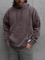 Hoodie de color marrón con efecto acid wash, capucha con cordones ajustables, bolsillo canguro frontal y pequeño estampado con texto en el pecho. Cuenta con una etiqueta decorativa en el borde inferior.