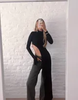 Top negro de manga larga con cuello alto y diseño asimétrico que deja al descubierto un costado del abdomen y cae en un panel largo hasta la rodilla o tobillo.