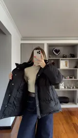 Campera puffer de corte holgado en color beige, con diseño acolchado, cuello alto y capucha desmontable. Cuenta con cierre frontal y botones a presión, además de puños elásticos.