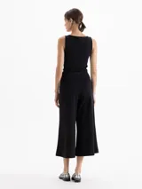 Pantalon de corte amplio y estilo culotte, confeccionado en tejido de punto color negro. Presenta cintura elastizada, cierre lateral y detalles de costuras verticales con pespuntes decorativos que recorren el frente de las piernas.