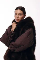 Campera de invierno con frente de piel sintética y capucha integrada, combinada con mangas acolchadas de estilo puffer en color marrón oscuro.