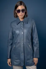 Campera de cuero en tono azul con efecto gastado, de corte recto y largo medio. Presenta cuello camisero, cierre frontal con botones a presión ocultos bajo una solapa y bolsillos laterales con cierre metálico.
