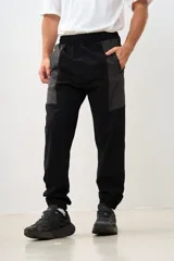 Pantalón de jogging negro con paneles grises en la parte superior, cintura elástica con cordón ajustable y puños elásticos en los tobillos.