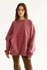 Buzo oversize de corte unisex, color rojo con efecto desgastado (acid wash), confeccionado en algodón con interior de polar. Presenta costuras frontales decorativas, hombros caídos, mangas largas con puños elastizados, rib en el cuello y el ruedo, y un pequeño logo bordado en el pecho.