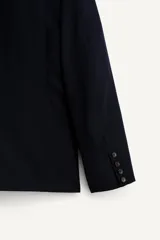 Blazer de corte relajado confeccionada en tejido con lana, color negro. Presenta cuello con solapas de muesca, cierre frontal de un botón y bolsillos de plastrón en la cadera. Destaca por su bordado en hilo dorado con motivos vegetales en la parte frontal.