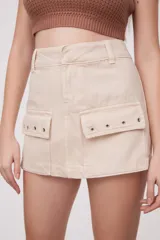 Falda corta de jean color beige claro, de corte al cuerpo, con tiro bajo y bolsillos cargo grandes y planos en los laterales.