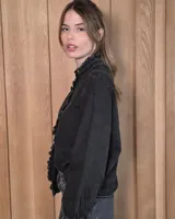 Camisa de denim negro con volados en el cuello alto y en la botonera frontal, manga larga con puños fruncidos y cierre de botones metálicos dorados.