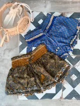 Short de seda con elástico fruncido en la cintura y volado en el ruedo. Presenta un estampado vibrante en tonos rojo/bordó y turquesa con motivos florales o arabescos.