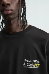 Camiseta negra de corte boxy fit, cuello redondo y manga corta, con estampado frontal en blanco y amarillo que dice "Social Media & Ciao Amore".
