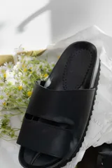 Sandalias tipo chinelas color negro con suela anatómica y diseño de banda ancha con abertura horizontal.