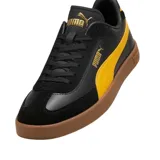 Championes Puma modelo Club Li Era, con diseño de perfil bajo en color negro, franja lateral blanca característica de la marca y suela de goma color caramelo. Presenta detalles en dorado en el logo lateral y la lengüeta.
